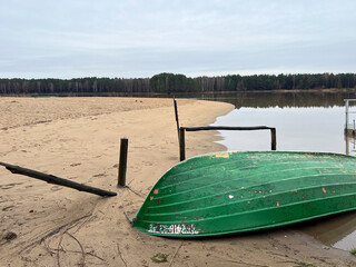 A boat lying upside down on the beach of a small lake in early spring after the snow and ice have gone - 778351477