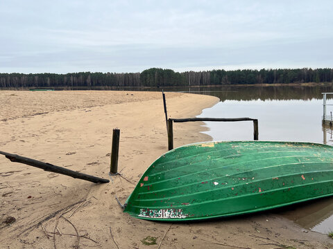 A boat lying upside down on the beach of a small lake in early spring after the snow and ice have gone