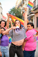 Fototapeta premium LGBTQ people with rainbow flags and a megaphone fighting for their rights. They are all smiling and celebrating Pride Parade.