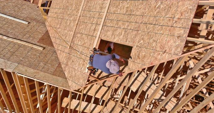 Carpentry construction worker hammers nail into plywood on roof of future home