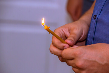 Male hands holding a holy candle in a church close-up