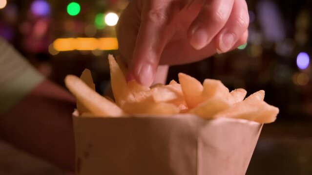 Man eats French fries from kraft paper bag in street food court close-up.