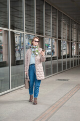 Beautiful stylish young woman with sunglasses and mobile phone walking near building with mirror wall