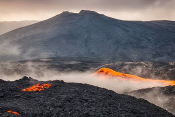 Steaming volcanic mountains pierce the clouds in an active geothermal island country