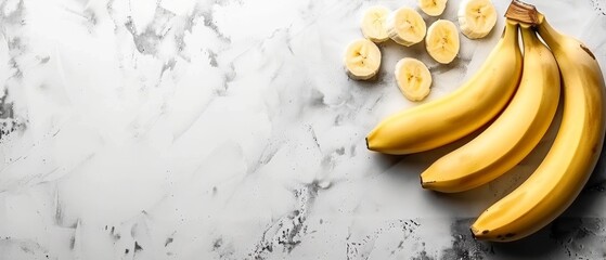   A few bananas are resting atop a marble countertop, alongside sliced chunks of banana