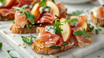 Delicious appetizer crostini, tapas, or open-faced sandwiches featuring pear, prosciutto, arugula, and blue cheese, elegantly arranged on a white marble board. T