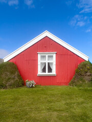 nordic style house with a high triangular gable to reduce snow adhesion The walls of the house are painted bright red. During the summer there is bright green grass surrounding the house.