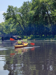 A teenage boy swims in a kayak on the river against the background of trees. Rear view