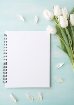 White tulips and petals on a blue wooden background with a blank notebook. Still life, floral, art, photography, interior, blue, white, spring.