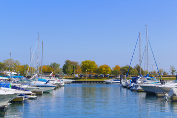 Fototapeta na wymiar Marina with docked yachts, boats, sailboats, motorboats and calm water against bright blue sky and autumn trees background .Picturesque urban landscape photo.
