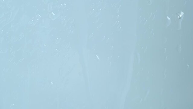Close-up of water droplets on window. Water drops in window on light blue background.