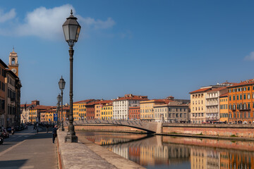 Arno river embankment with bridge and buildings of old city reflections in water at day, Pisa, Italy - obrazy, fototapety, plakaty