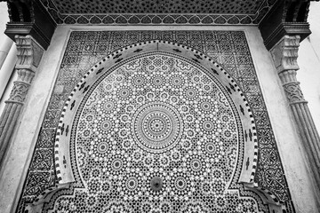 A monochrome filtered image of detailed islamic geometrical mosaic patterns cover a wall with the...