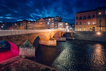 A historic landmark spanning the Miljacka River, bathed in the twilight glow of the evening,...