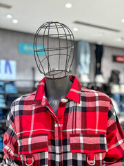 A mannequin wearing a red plaid shirt is displayed in a store