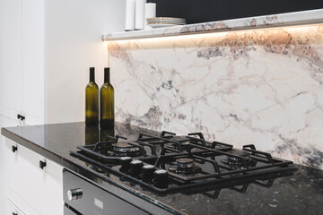 A black stove top with four burners and a marble counter top. A bottle of wine is on the counter...