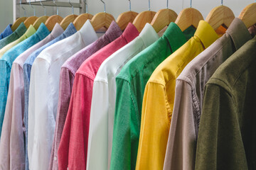 A row of shirts hanging on a rack, with the colors ranging from white to green. The shirts are neatly folded and arranged in a row - obrazy, fototapety, plakaty