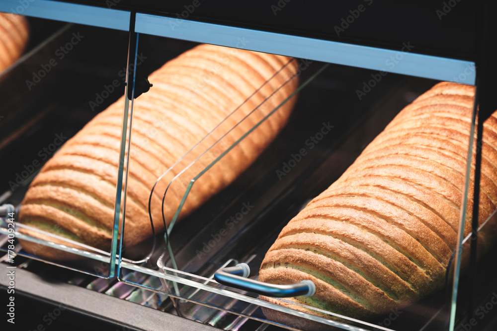 Poster a row of bread loaves are displayed in a glass case. the bread is golden brown and he is freshly bak