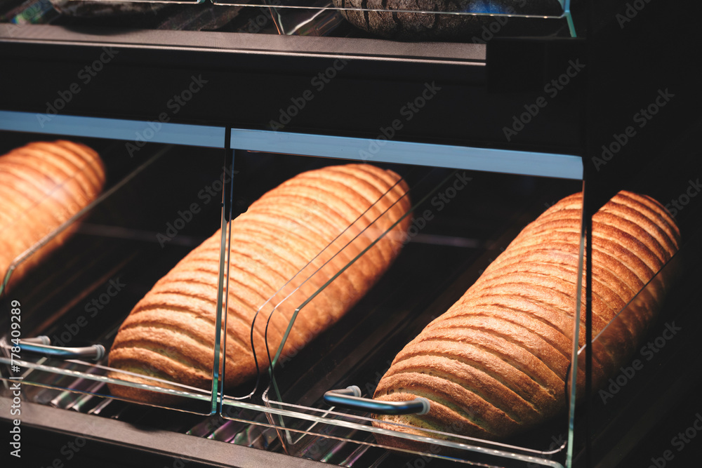Poster a row of bread loaves are displayed in a glass case. the bread is golden brown and he is freshly bak