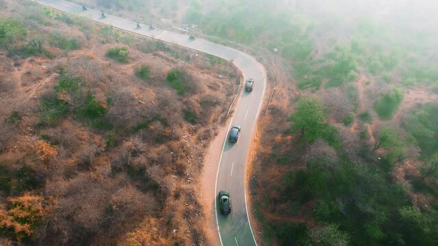 aerial drone shot of cars driving along narrow winding road, multiple bikes, two wheelers, with barren rocks on both sides in aravalli mountains in gurgaon rajasthan India