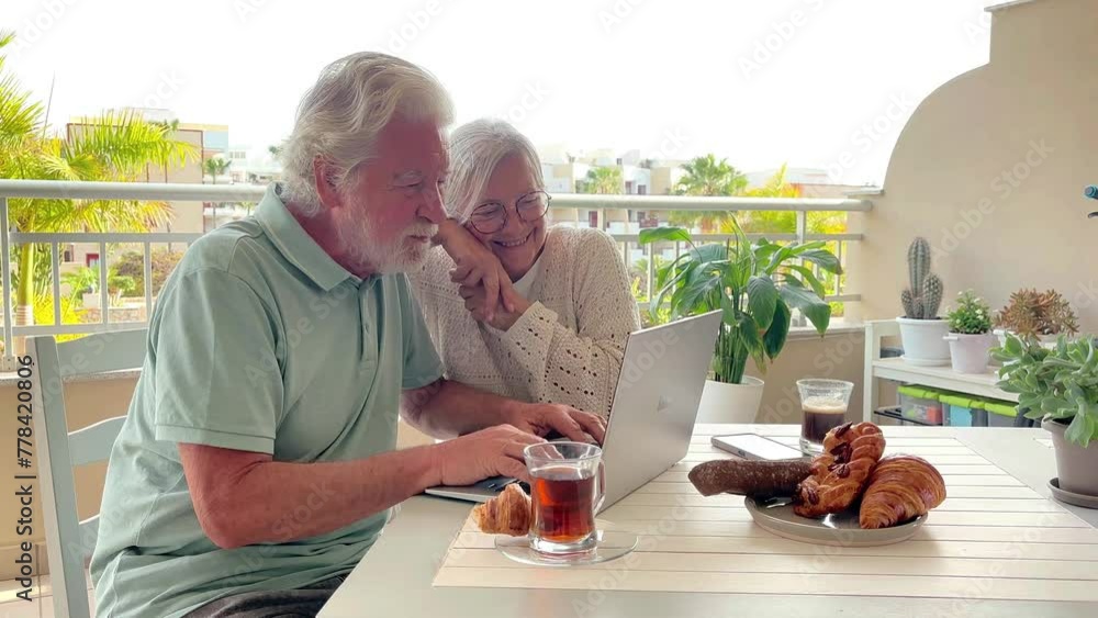 Sticker Cheerful senior couple using laptop enjoying technology, elderly 70 years old caucasian people sitting outdoors on terrace browsing, shopping on line, follow social media together