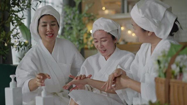 Smiling asian middle aged women apply cream on her arm and feel good.Asia women friends relaxing enjoy and spa massage with cream on her arm put on bathrobe.Spa beauty massage healthy wellness.