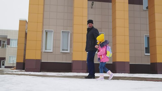father leads girl daughter school walking along winter road, child kid girl daughter holds father hand way school, school children bag, road school, girl goes class lesson, educational children