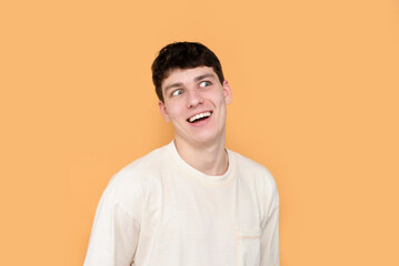 A young guy in a white T-shirt on a yellow background is fooling around, having a lot of fun, rolling his eyes. A cheerful guy with a funny face