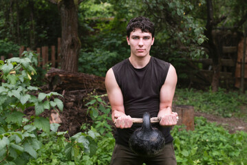 Young guy in the nature in the forest lifting a heavy weight on his biceps, the guy likes to exercise in the fresh air, avoids gyms and large crowds