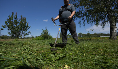 On a sunny day, a man mows the grass on his front lawn with a trimmer. An electric trimmer deftly...