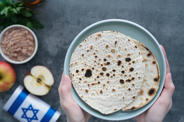 Human hands holding handmade round Matzah in a plate on a concrete background. Saved Jewish Pesach Tradition. Jewish Passover celebrations. top view