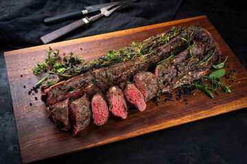 Traditionally roasted saddle of venison with fillet pieces and herbs served as close-up on a wooden...