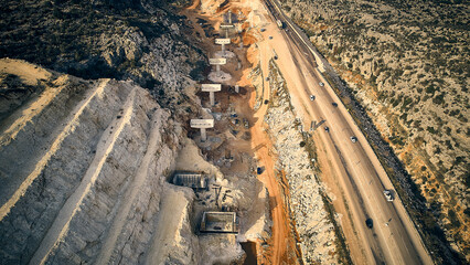 Aerial view of highway ledges under construction after drilling and blasting operations. Road construction at rough highland terrain. Supports of bridge overpass under construction