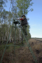 A stout man climbs into a hunter's high stand in a beautiful bog area