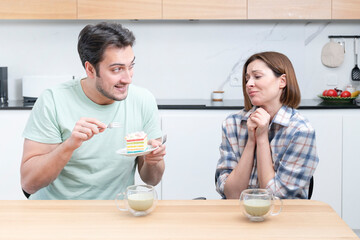 A young couple is sitting in the kitchen and ready to eat a delicious cake	