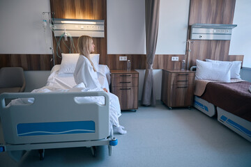 Dejected female patient sitting alone in comfortable hospital room