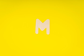 Letter M in wood on yellow background