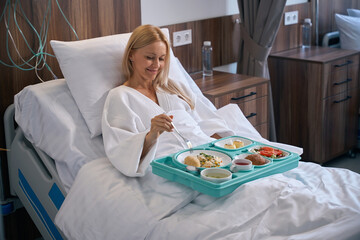 Pleased recumbent patient is having lunch in private clinic ward - 778470622