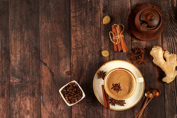 Poster Cup of coffee with milk, ginger, anise and cinnamon on an old wooden table. Traditional Indian drink with spices, cafe concept, advertising for restaurant and menu. © Светлана Балынь