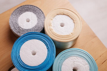 A set of four ribbon spools in soft pastel and metallic shades, arranged on a wooden surface.