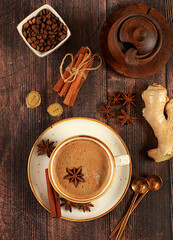Cup of coffee with milk, ginger, anise and cinnamon on an old wooden table. Traditional Indian drink with spices, cafe concept, advertising for restaurant and menu.