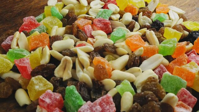 Mix of multi-colored dried fruits and nuts scattered on the surface, rotating in a circle. Medium plan