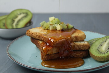 Healthy breakfast at the hotel. Toast with honey and pieces of fruit and kiwi on grey background
