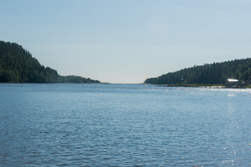 View of the bay surrounded by hills with a forest and a fishing village, against a clear blue sky