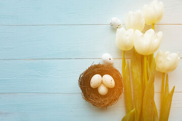 White tulips and quail eggs in the neast on wooden background - Easter concept. Top view, copy...