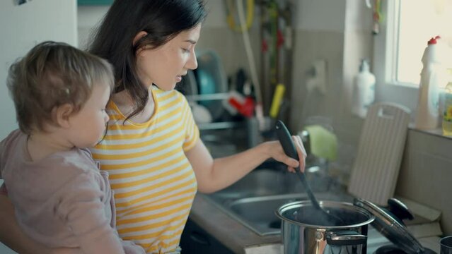 Cinematic authentic shot of happy mother and her little toddler baby boy son are having fun to make dough with flour together for baking cookies or bread in kitchen at home.