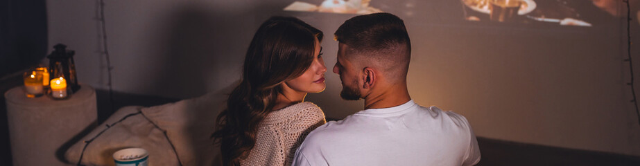 Banner. Romantic surprise for girlfriend or boyfriend on Saint Valentine's Day. Bedroom prepared for watching old movies, decorated with lights and burning candles. Cozy home Christmas atmosphere