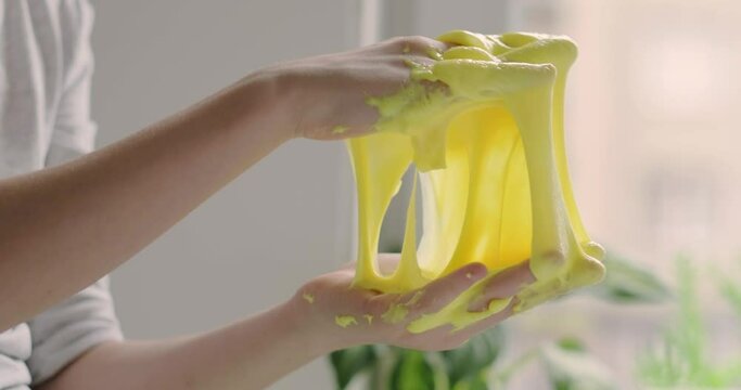 Little girl stretches yellow slime to the sides, hands close up stretching vibrant yellow slime, creative and fun concept for educational activities, crafting blogs, and playing toy at home
