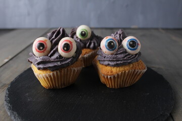 Cupcakes cakes with black grey cream and eyes on grey background with space for text. Preparing the concept of the Halloween holiday