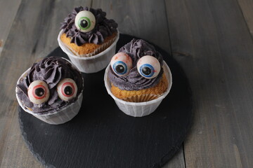 Three cupcakes with grey black cream and eyes. Halloween Holiday Preparation Concept
